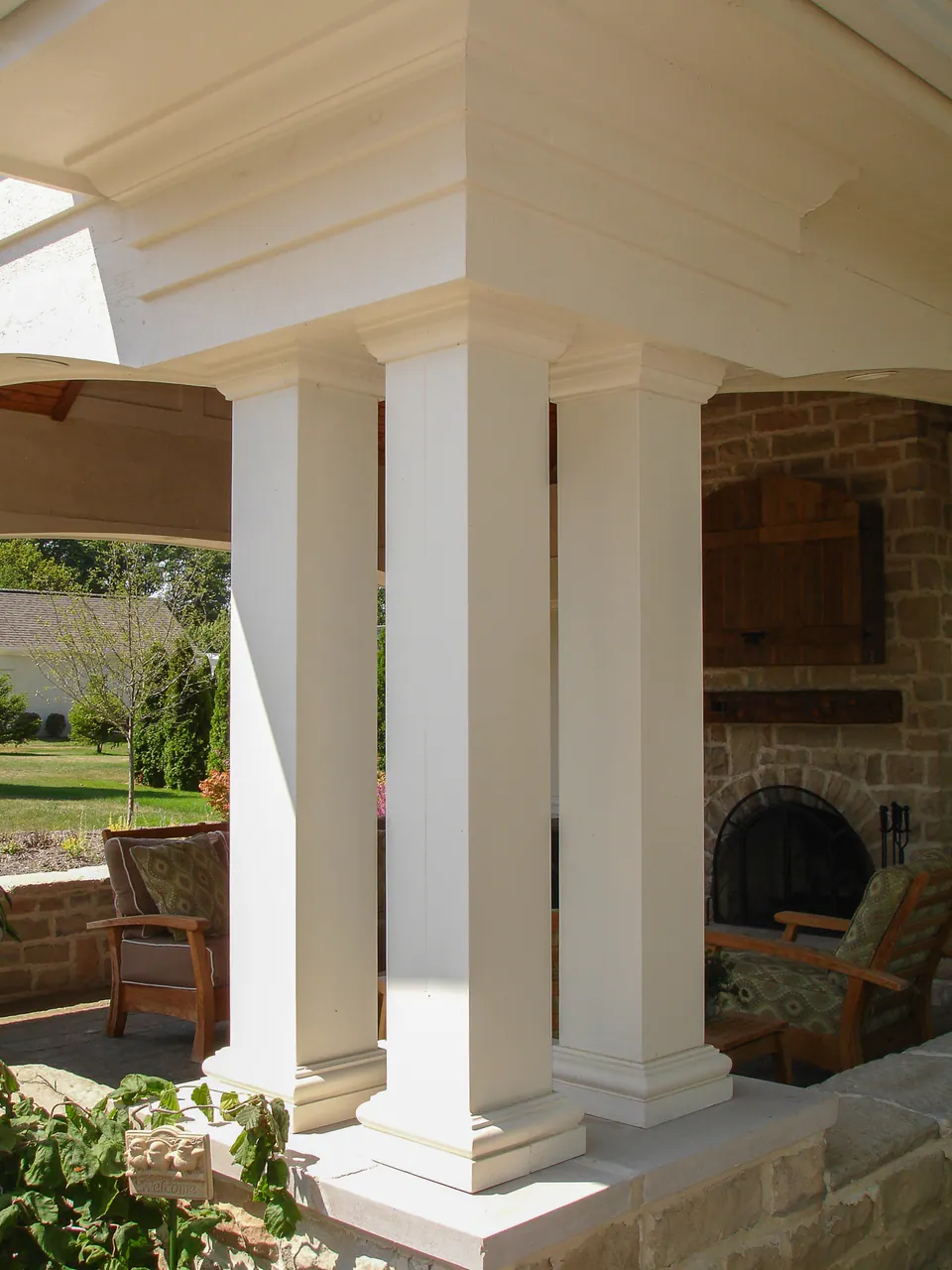 Close view of pavilion columns, stone fireplace, paver floor, and garden planting outside the covered room.